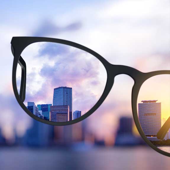 A blurred city skyline with in focused areas viewed through a held up pair of glasses